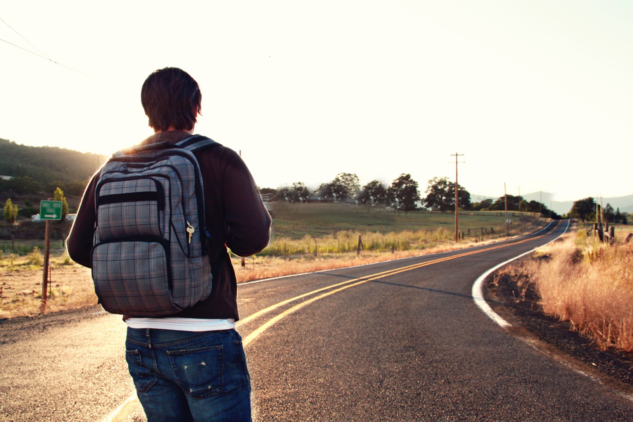 A man with a backpack walking down a road